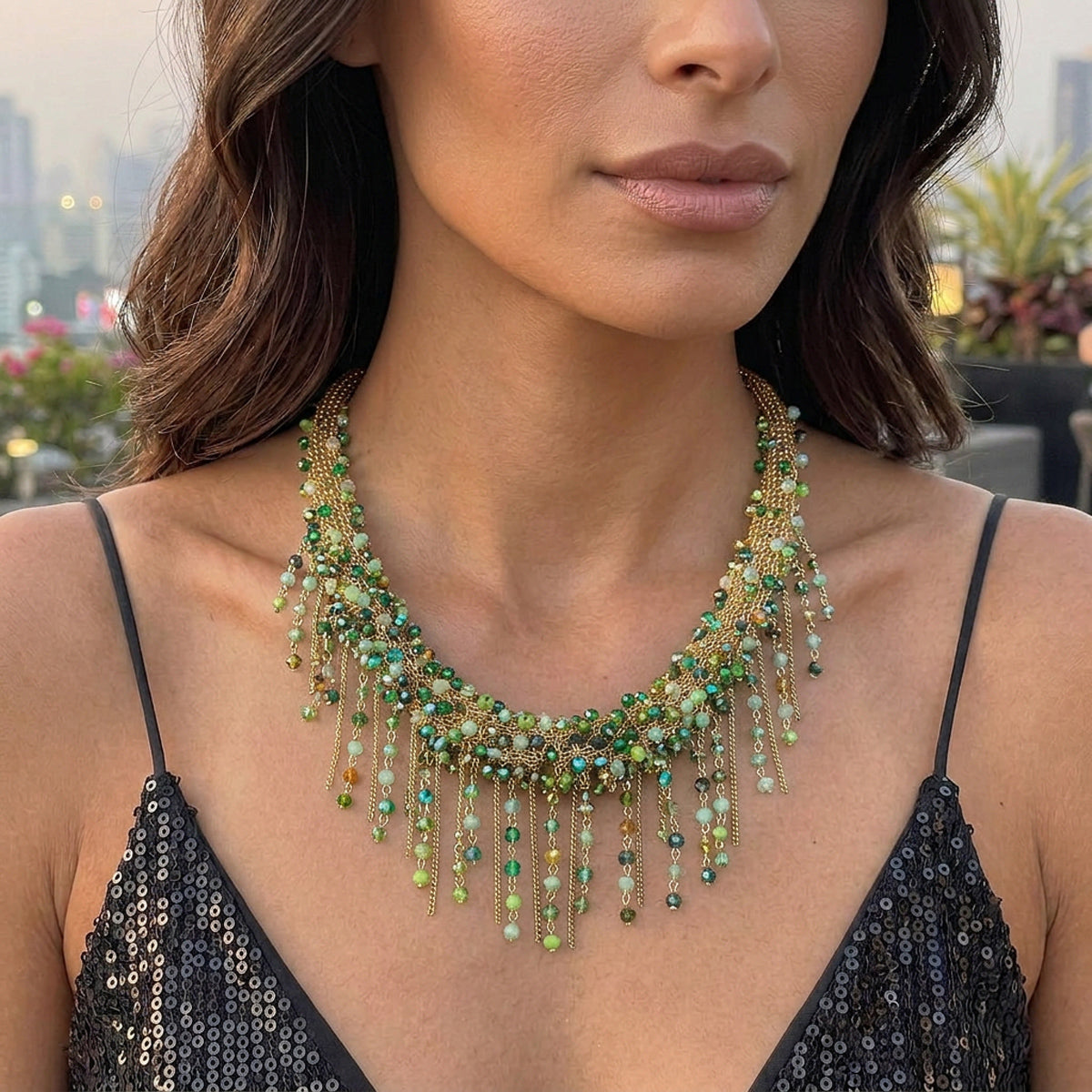 A close-up lifestyle shot of a woman wearing a chunky, ornate bohemian-style statement necklace. The necklace features a gold-tone chain structure adorned with green beads, clear faceted beads, and dangling chains.