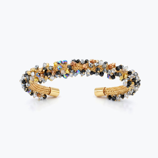 Gold cuff bracelet with a handknitted wire band decorated with metallic black, bronze, and silver crystals.