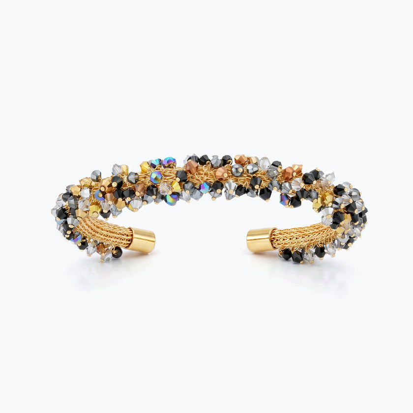 Gold cuff bracelet with a handknitted wire band decorated with metallic black, bronze, and silver crystals.