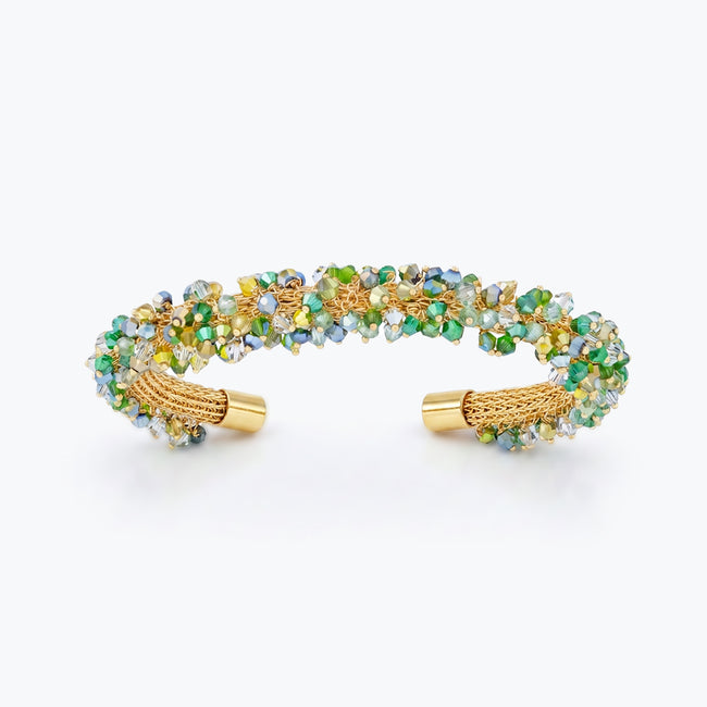 Gold cuff bracelet featuring a handknitted wire mesh design studded with emerald green premium crystals.