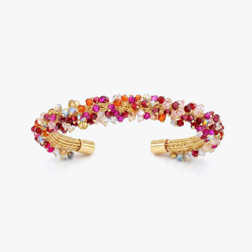 Gold cuff bracelet showing a handknitted wire mesh structure lined with red and pink premium crystals.