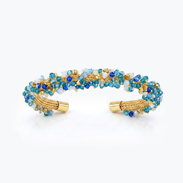 Gold cuff bracelet featuring a handknitted wire mesh band set with blue and aqua reflective crystals.