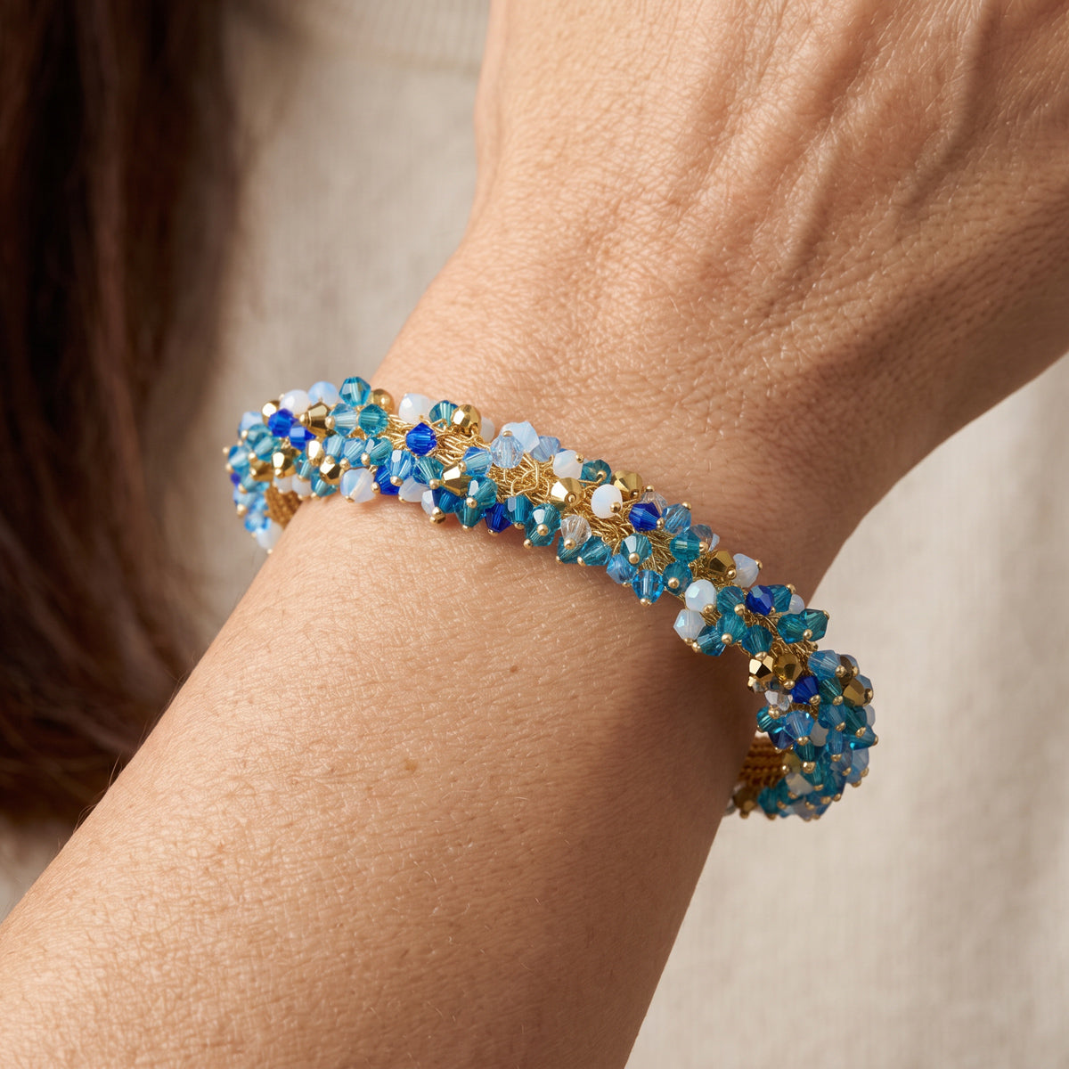 A close-up of a beaded bracelet worn on a person's wrist. The bracelet features light blue, medium blue, and dark blue faceted beads, white beads, and gold-toned metal settings.