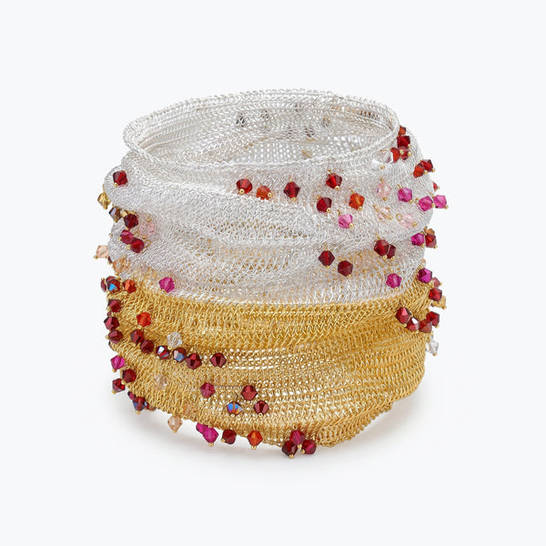 Silver gold distorted cuff bracelet showing a slender handknitted wire structure finished with rows of pink and red crystals.