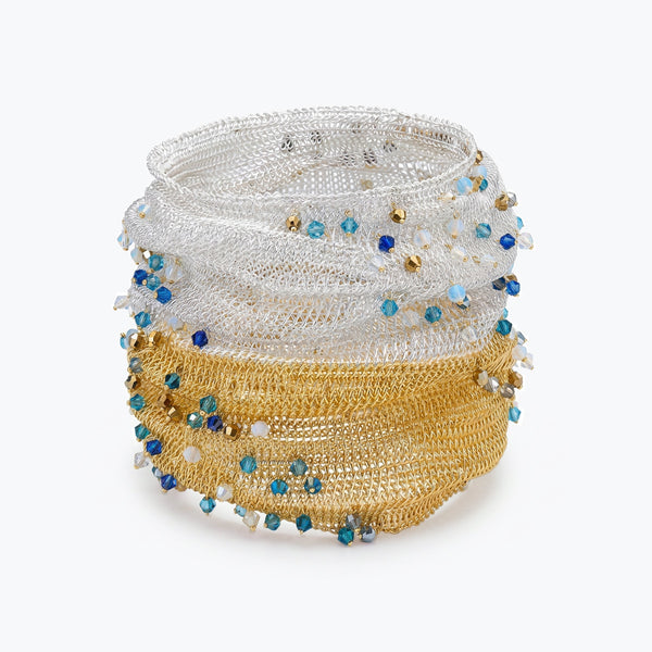 Silver gold distorted cuff bracelet with a slender handknitted wire pattern accented by light blue and silver reflective crystals.