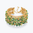 Gold cuff bracelet featuring a textured handknitted wire band studded with emerald green premium crystals.