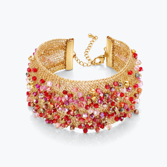 Gold cuff bracelet showing a textured handknitted wire structure finished with rows of red and pink premium crystals.