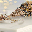 Gold drop earrings composed of handknitted wire cone and individually hanging gunmetal, bronze, and black premium crystals.