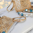 Gold drop earrings with a diamond-shaped handknitted wire mesh square panel and cascading strands of blue reflective crystals.
