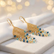 Gold drop earrings with a diamond-shaped handknitted wire mesh square panel and cascading strands of blue reflective crystals.
