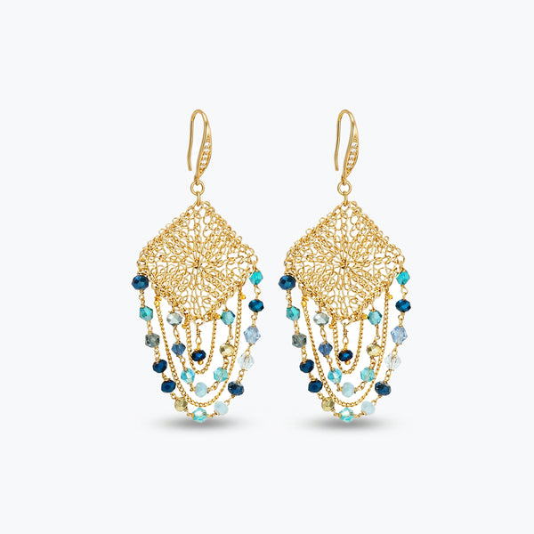 Gold drop earrings with a diamond-shaped handknitted wire mesh square panel and cascading strands of blue reflective crystals.
