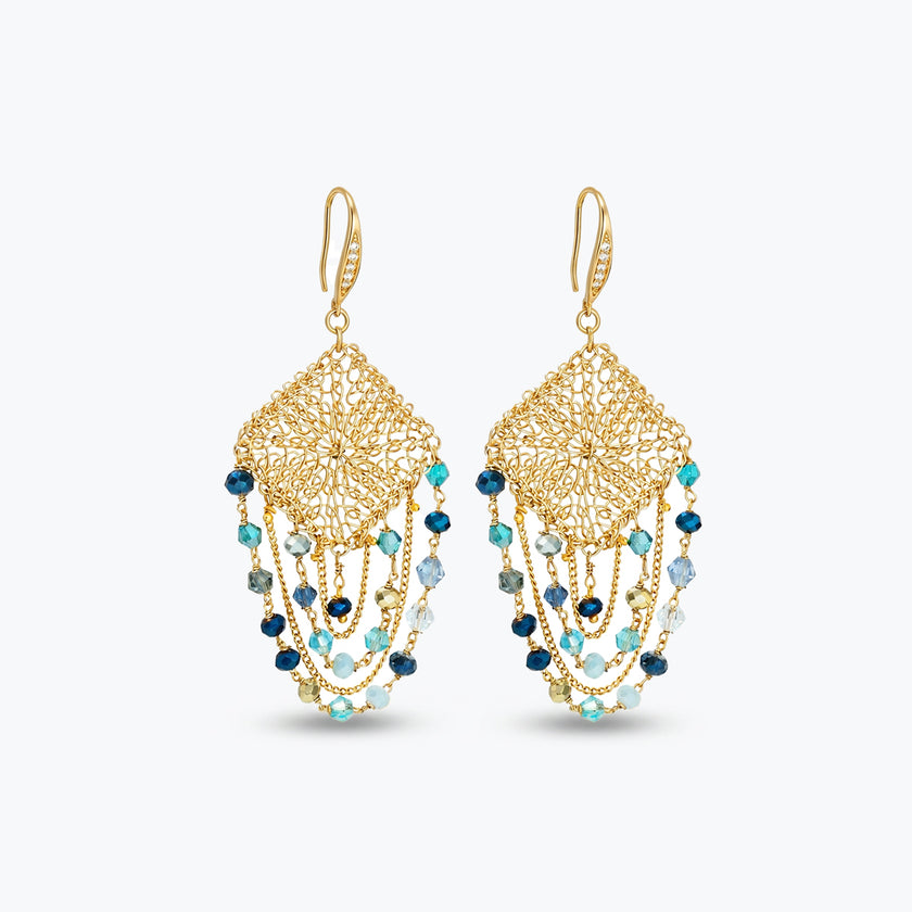 Gold drop earrings with a diamond-shaped handknitted wire mesh square panel and cascading strands of blue reflective crystals.
