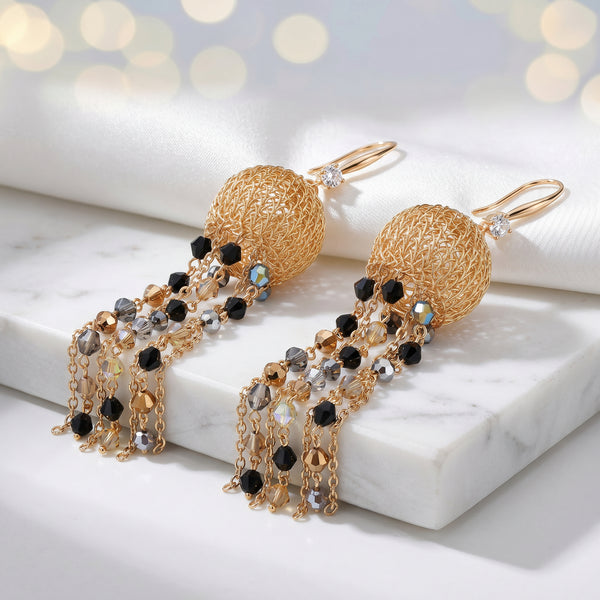 Gold drop earrings featuring a sphere-shaped handknitted wire shape and tassel strands of black and bronze crystals.