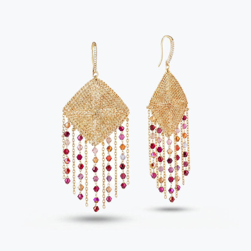 Gold drop earrings showcasing a handknitted wire rhombus panel housing bright pink and red reflective crystals.