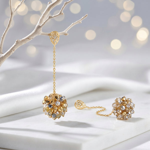 Gold drop earrings displaying a  handknitted wire mesh ball and clusters of clear and gold premium crystals.
