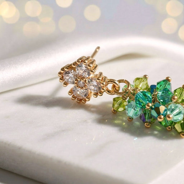 Gold drop earrings with a vertical handknitted wire mesh strip trailing down into green individually hanging crystals.

