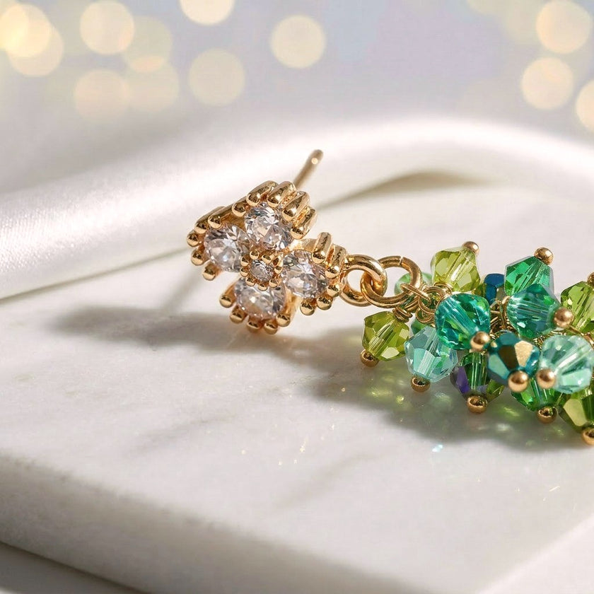 Gold drop earrings with a vertical handknitted wire mesh strip trailing down into green individually hanging crystals.
