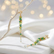 Gold drop earrings with a vertical handknitted wire mesh strip trailing down into green individually hanging crystals.
