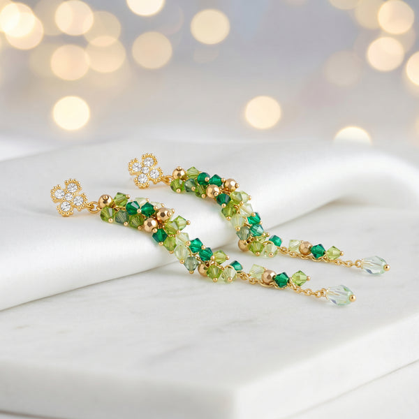 Gold drop earrings with a vertical handknitted wire mesh strip trailing down into green individually hanging crystals.
