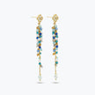 Gold drop earrings with an elongated handknitted  wire mesh bar holding strands of blue reflective crystals.
