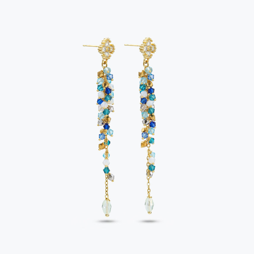 Gold drop earrings with an elongated handknitted  wire mesh bar holding strands of blue reflective crystals.
