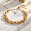 A gold-toned beaded bracelet with multiple strands of faceted clear and amber beads, displayed on a white marble surface with soft shadows.