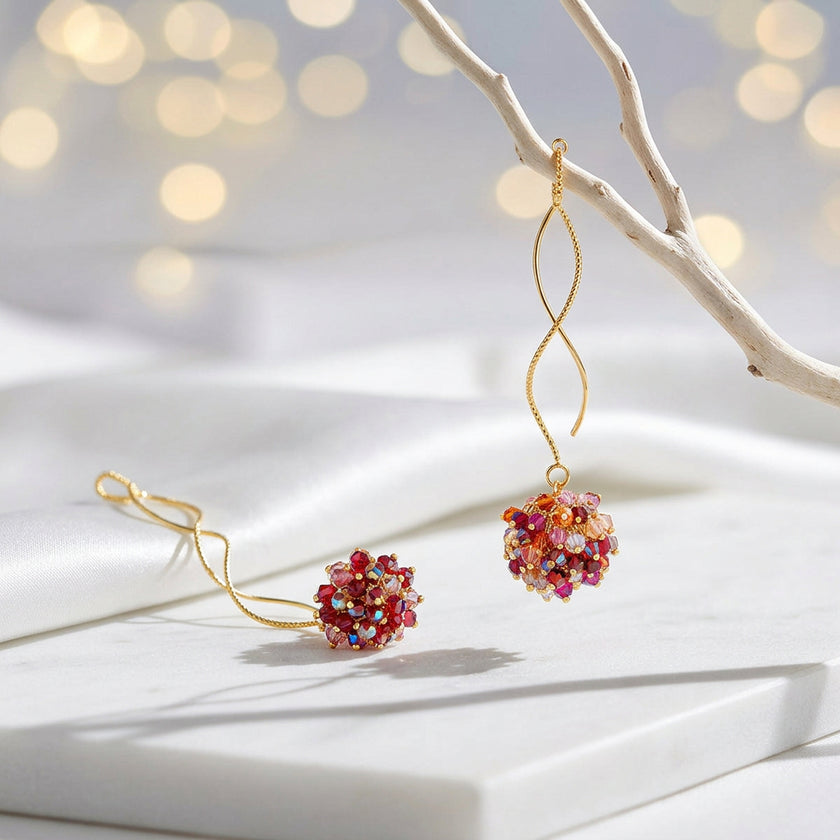 Gold spiral drop earrings with a rounded bunch of premium crystals in red, pink, and orange tones.