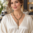 A woman wearing a luxurious gold-plated Y-necklace adorned with black and gold beads, set against a softly blurred indoor background.