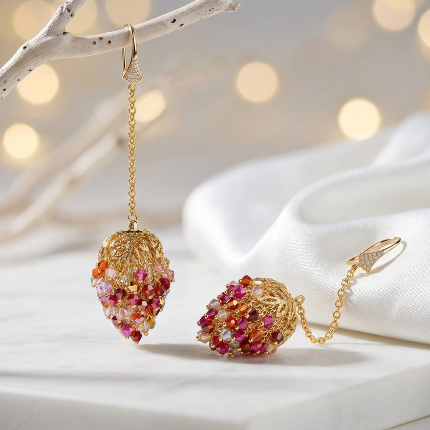 Long gold drop earrings featuring a handknitted wire mesh pod tightly packed with red and pink premium crystals.
