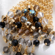 Gold drop earrings displaying a handknitted wire mesh triangle holding metallic black, gray, and bronze premium crystals.