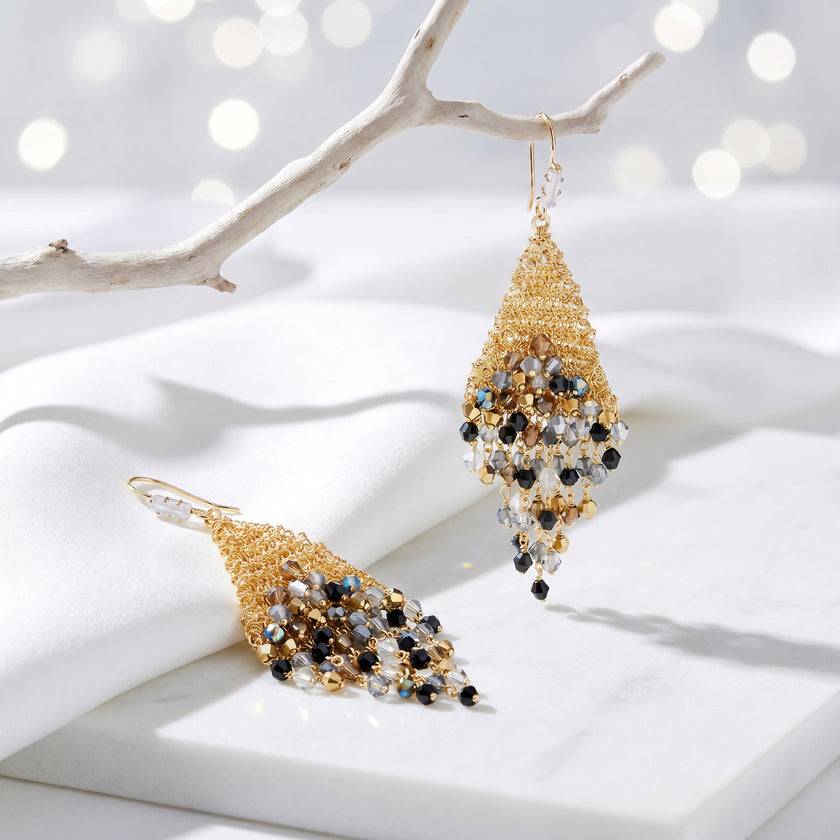 Gold drop earrings displaying a handknitted wire mesh triangle holding metallic black, gray, and bronze premium crystals.