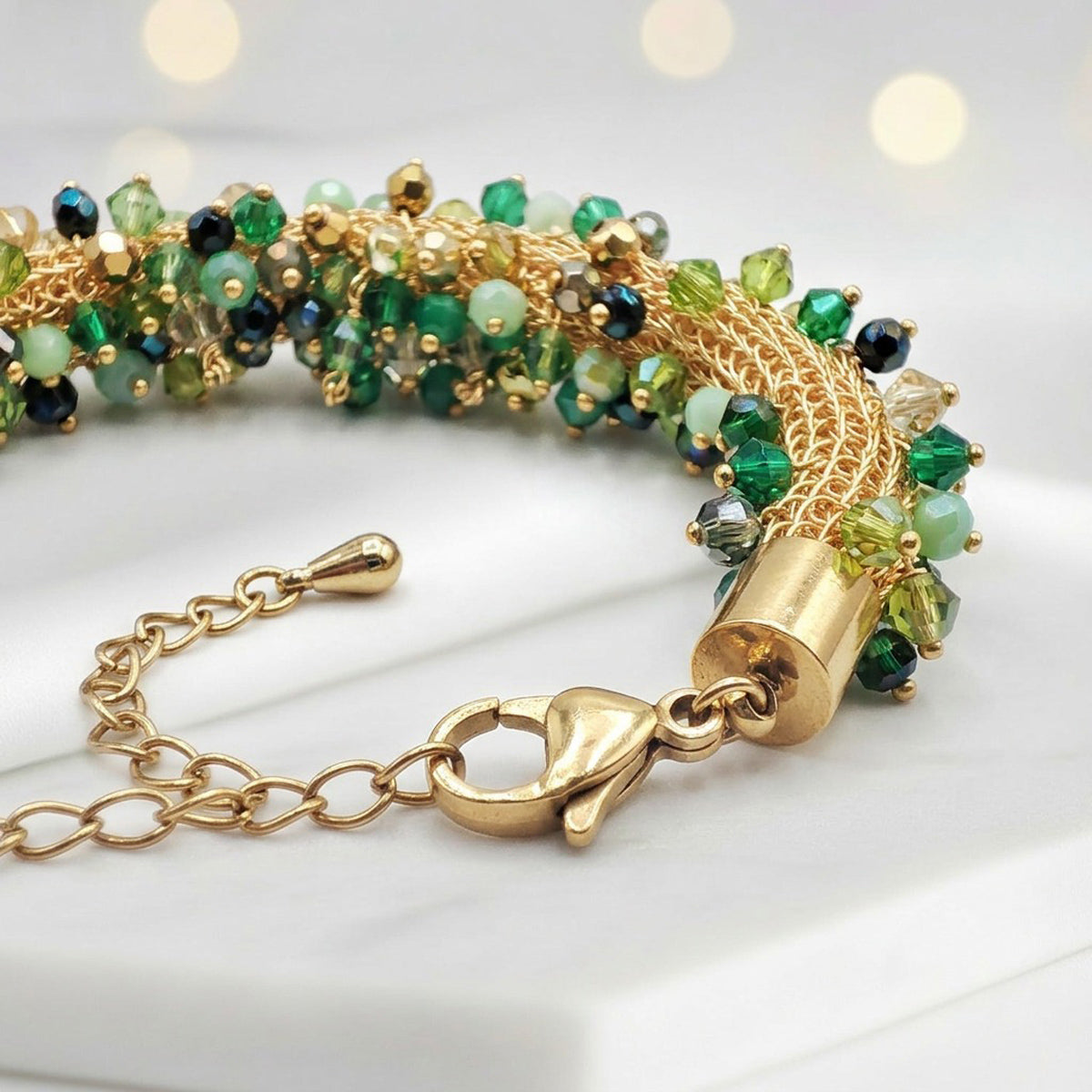 A gold-plated beaded bracelet with green and light blue beads, displayed on a white surface with a gold lobster clasp and extension chain.