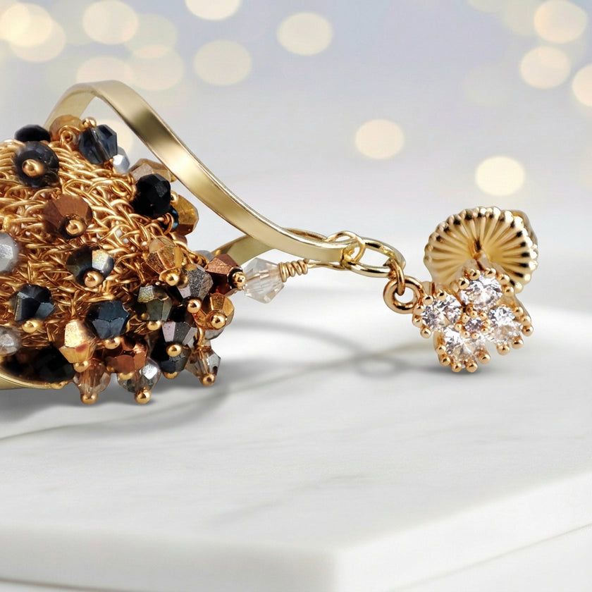 Gold drop earrings with an octagonal handknitted wire mesh base and hanging bronze, gray, and black crystals.
