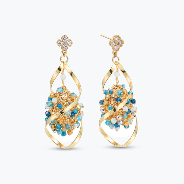 Gold drop earrings featuring an octagonal handknitted wire mesh panel holding blue and gray reflective crystals.
