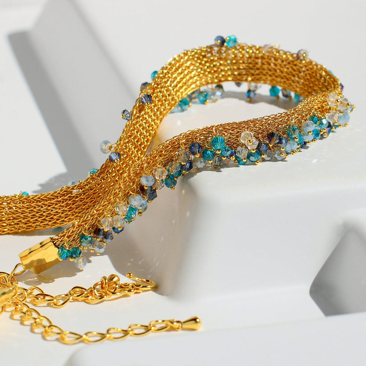 Gold bracelet with blue and green gemstones on a white background