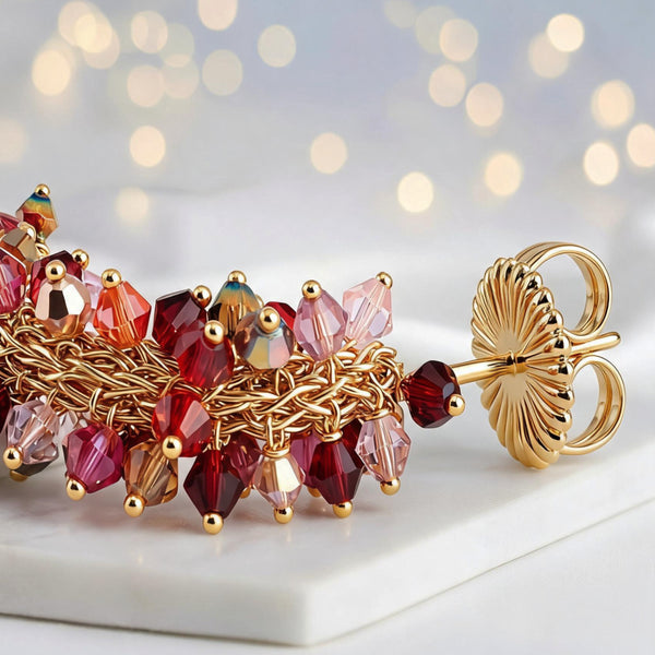 Gold loop earrings displaying a sunburst handknitted wire mesh frame filled with hanging pink and red crystals.
