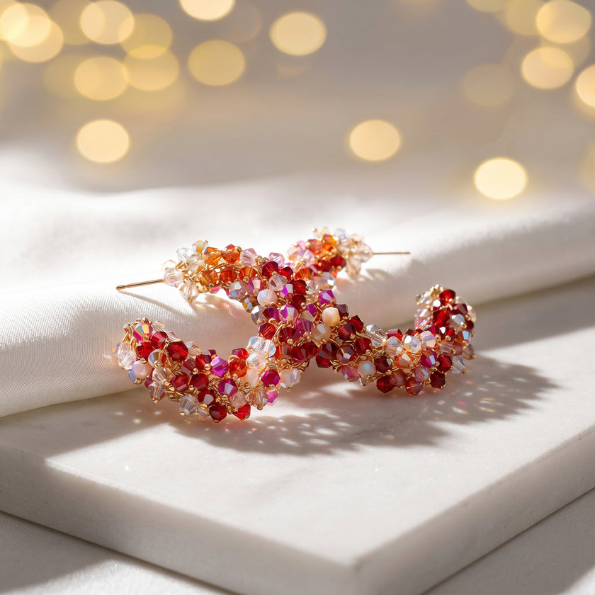 Gold loop earrings displaying a sunburst handknitted wire mesh frame filled with hanging pink and red crystals.

