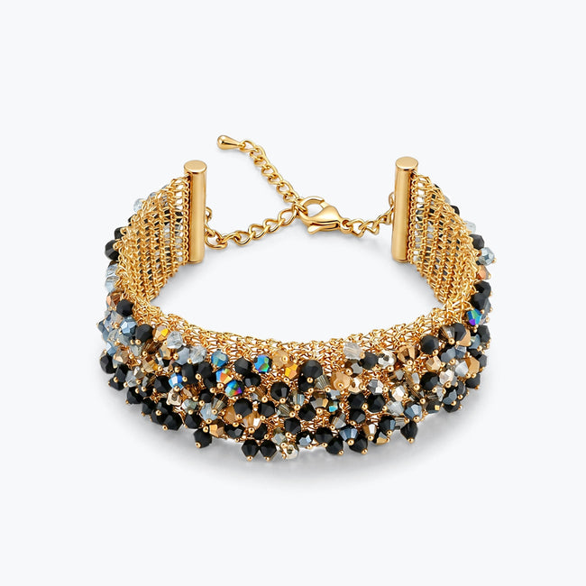 Gold ribbon bracelet displaying a wavy handknitted wire base decorated with black, bronze and silver reflective crystals.
