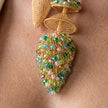 Close-up of a gold-tone beaded teardrop earring with green, blue, and clear faceted beads, worn on a person's ear lobe.